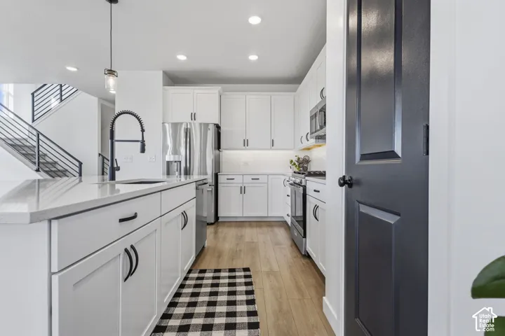 Modern kitchen featuring white cabinetry, stainless steel appliances, and wood-finish flooring