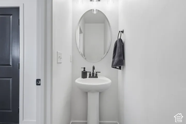 Pedestal sink with a matte black faucet, wall-mounted oval mirror, and a black paneled door