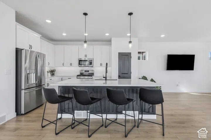 Kitchen featuring white cabinetry, stainless steel appliances, a center island with seating, pendant lighting, and wood-finish flooring