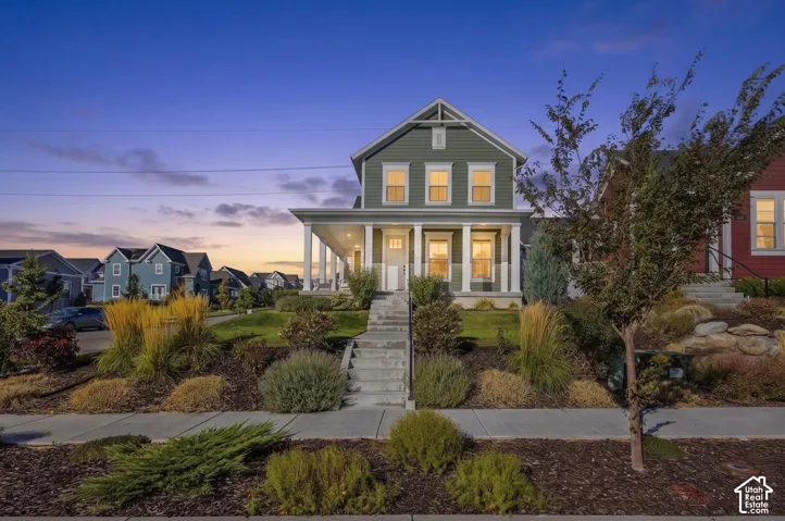 Gable roofline, covered front porch with white columns, concrete steps, and established landscaping