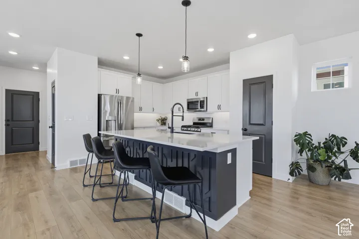 Gourmet kitchen with white cabinetry and stainless steel appliances, central island with seating, pendant lighting, and wood-finish flooring