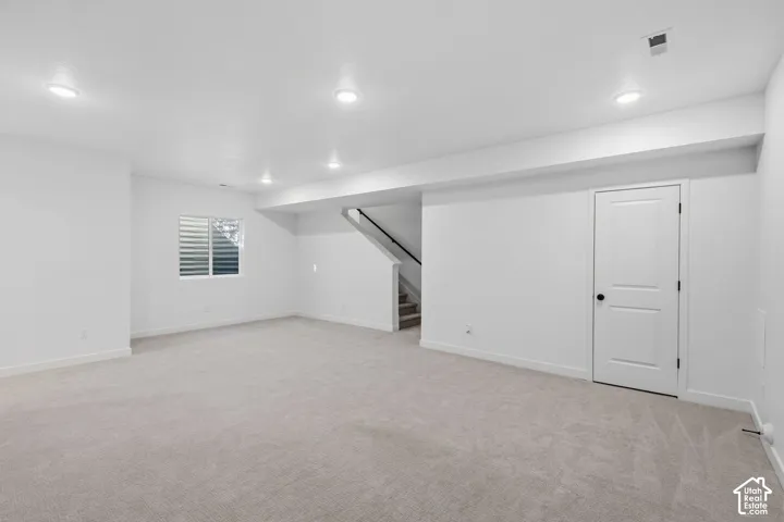 Expansive carpeted area with recessed lighting, large window with blinds, and white paneled door