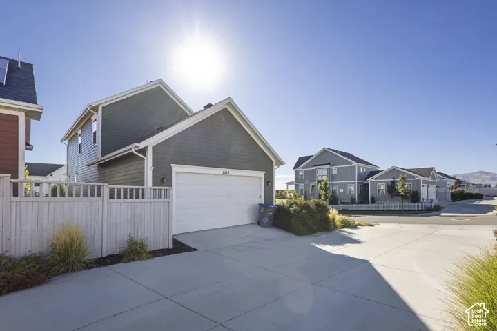 Two-story exterior with dark green horizontal siding, white garage door, concrete driveway, and light wood-tone fencing
