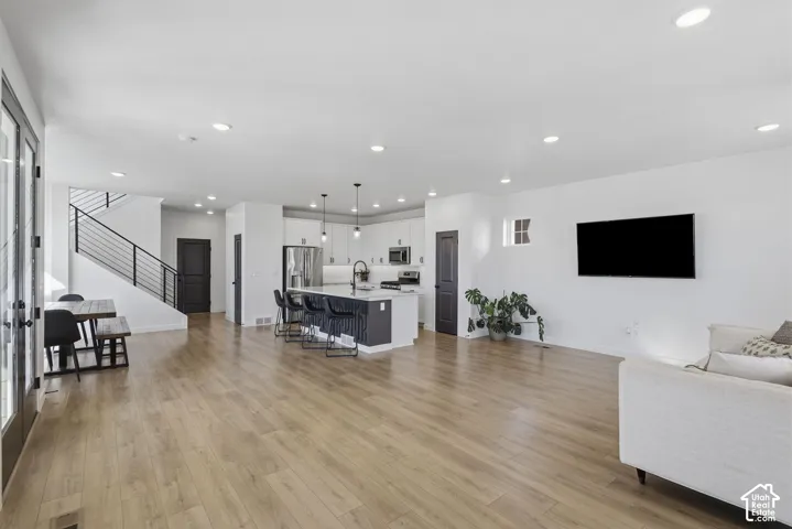 Open-concept living space with wood-finish flooring, a contemporary kitchen island, white cabinetry, and recessed lighting