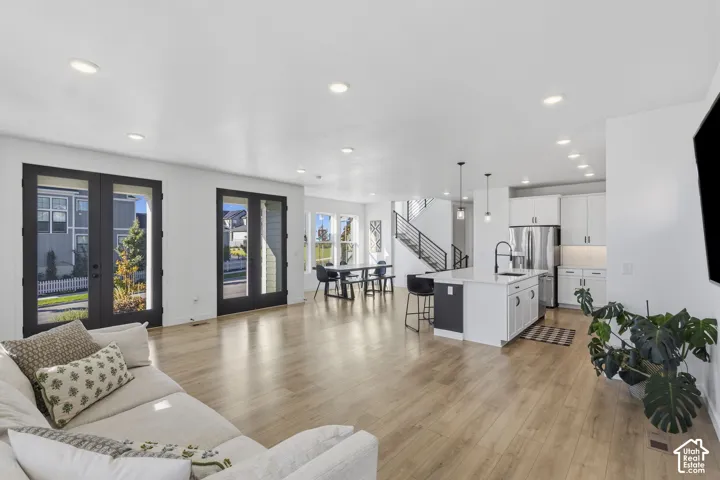 Light wood-finish flooring, recessed ceiling lighting, kitchen island with seating, stainless steel appliances, and a modern staircase with open risers