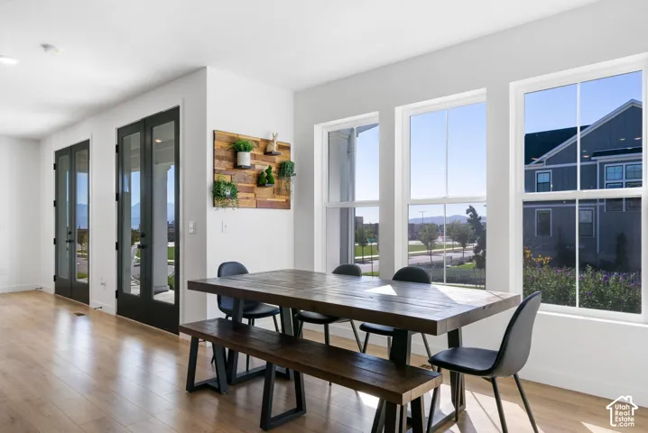 Wood-finish flooring throughout, multiple paneled glass doors with matte black hardware, and an abundance of natural light from large windows