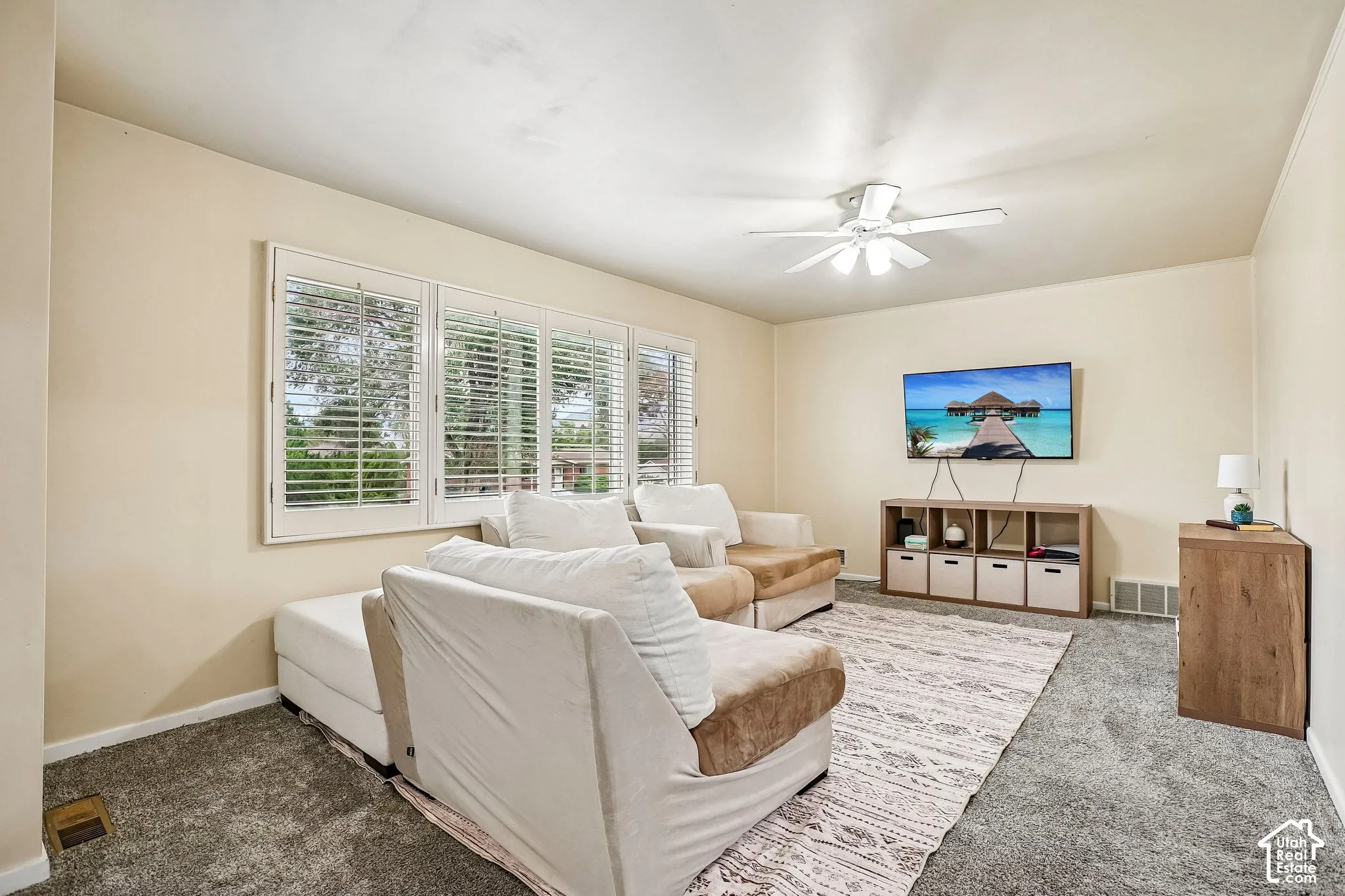 Living room with neutral wall color, white ceiling fan, and grey carpet flooring
