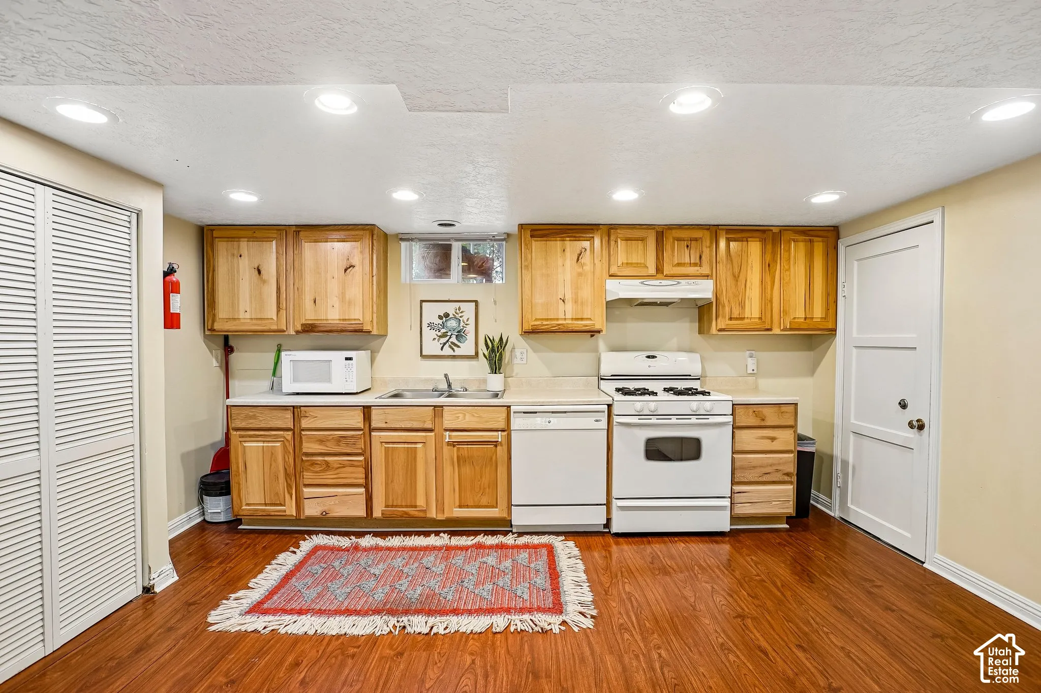 Wood-finish flooring, recessed lighting, wood cabinetry, white appliances, and a built-in sink