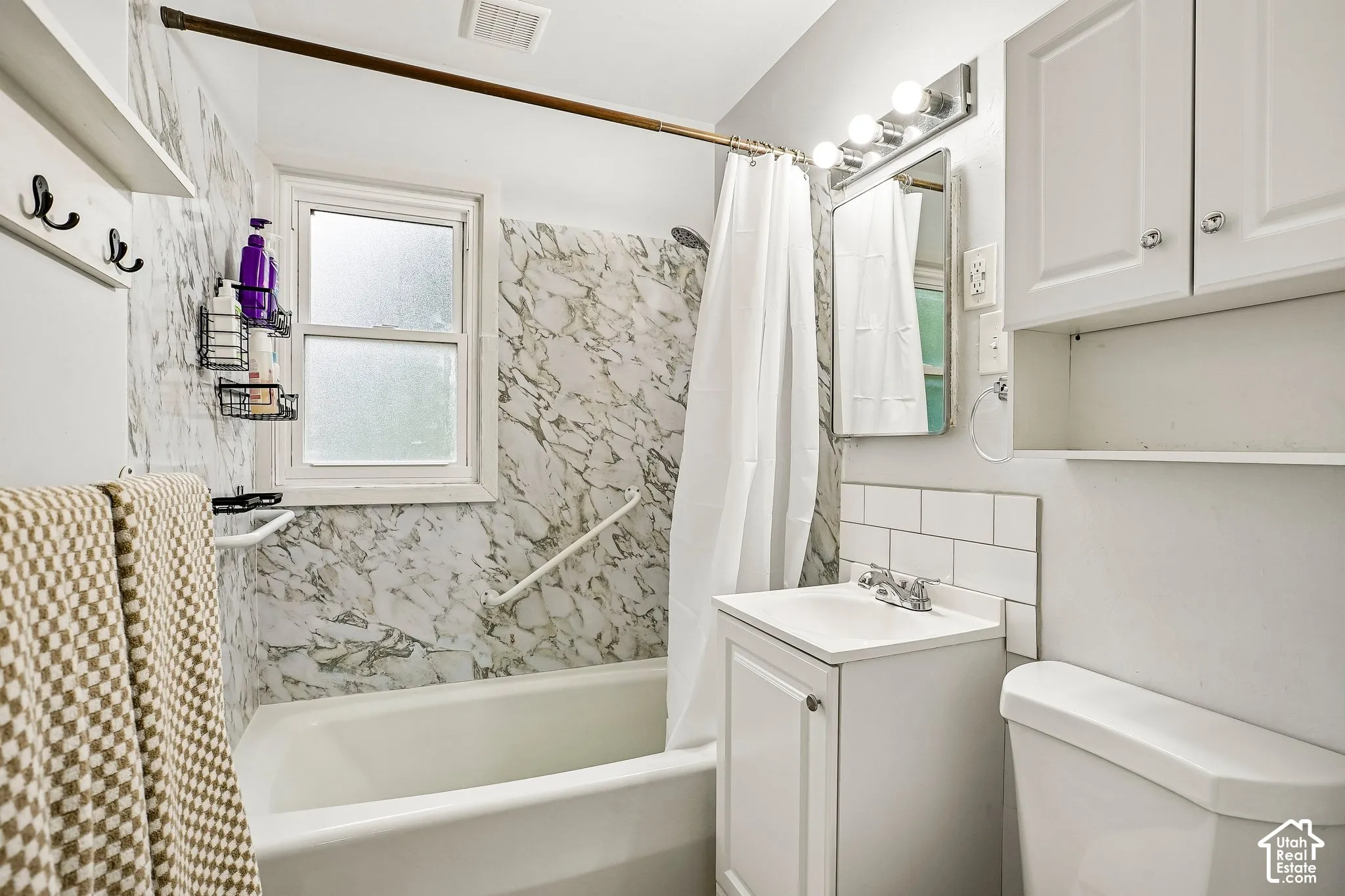 Bathroom featuring a tub/shower combination with marble-patterned surround, white subway tile backsplash, and a white vanity with integrated sink