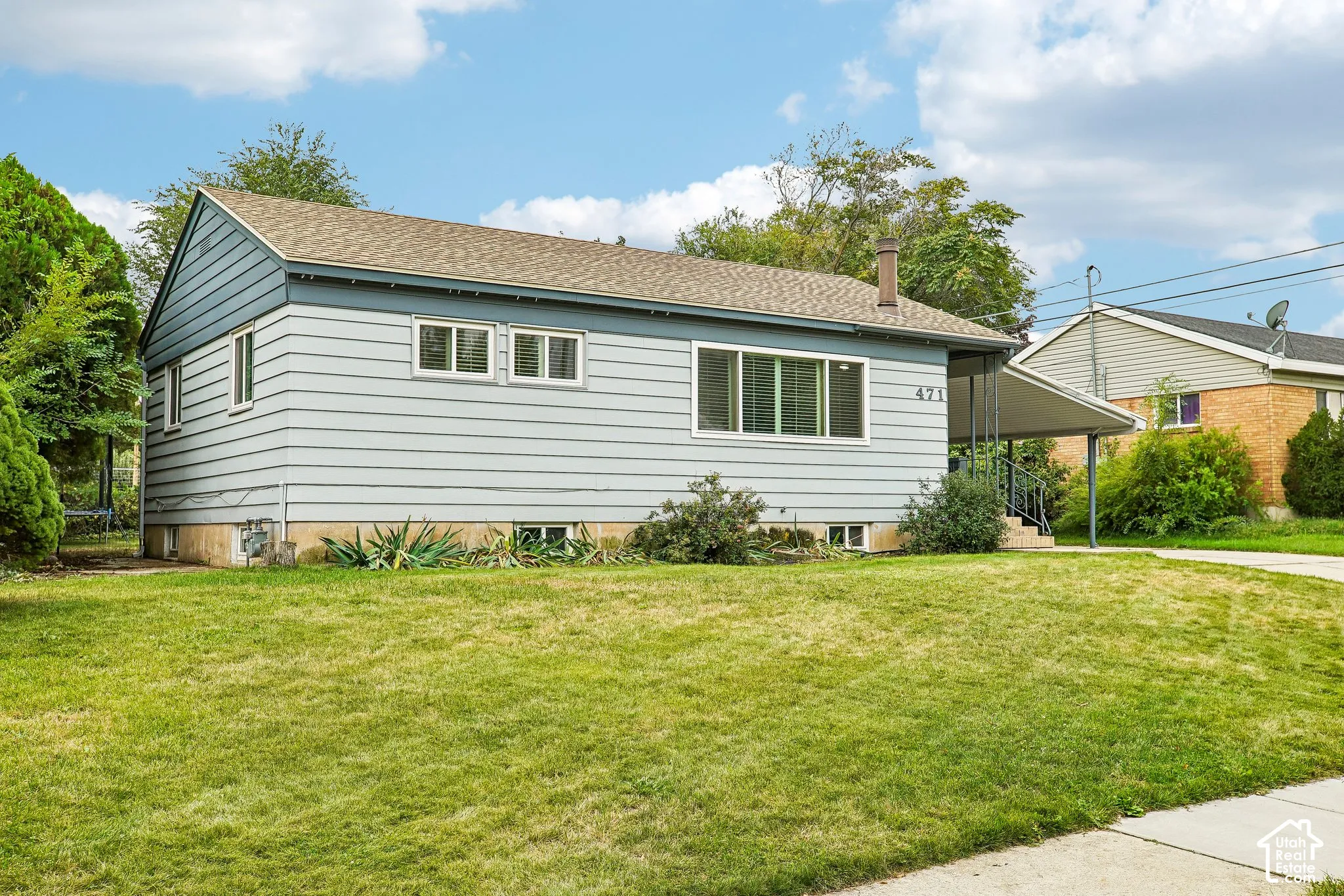 Single-story residence featuring light blue siding, a covered entry, and a front lawn with established landscaping