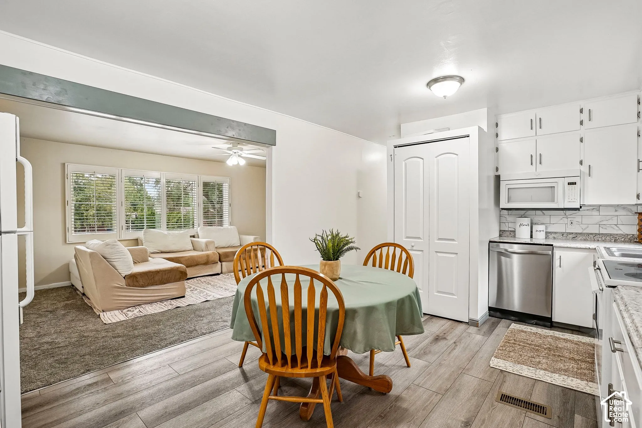 Kitchen with wood-finish flooring, white cabinetry, stainless steel dishwasher, and a white tile backsplash