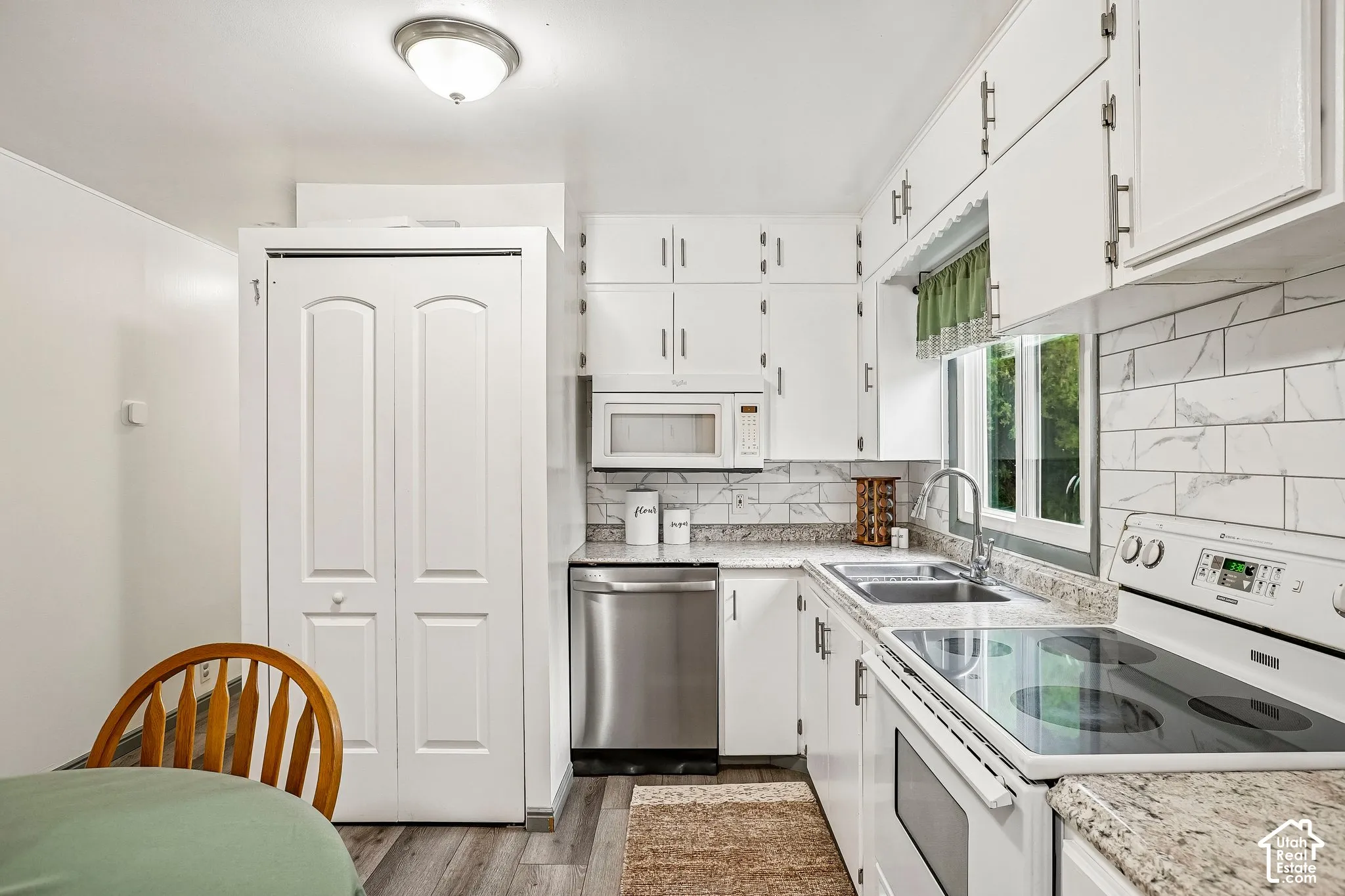 Kitchen featuring white cabinetry, light-toned countertops, a stainless steel dishwasher, and a tile backsplash