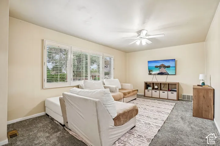 Living room with neutral wall color, white ceiling fan, and grey carpet flooring