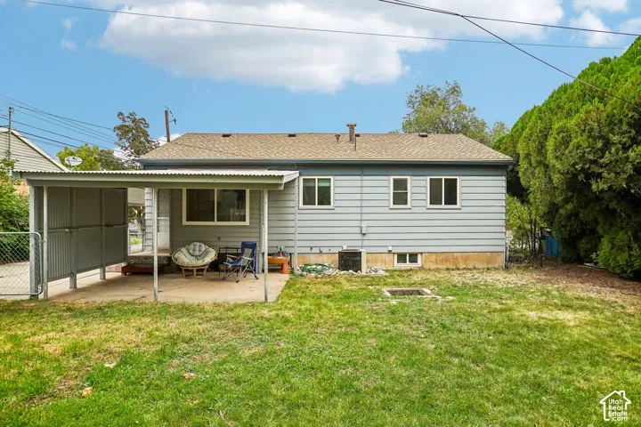 Expansive backyard featuring a manicured lawn, established perimeter trees, and a covered patio with direct access to the residence