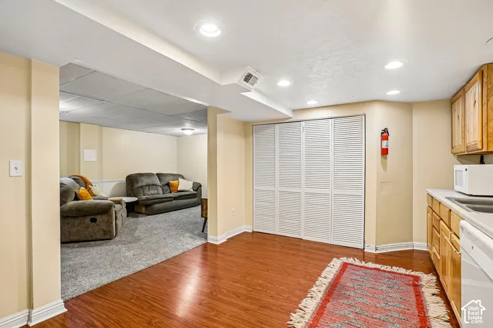 Wood-finish flooring, recessed lighting, white louvered bifold doors, and a built-in kitchenette with wood cabinetry
