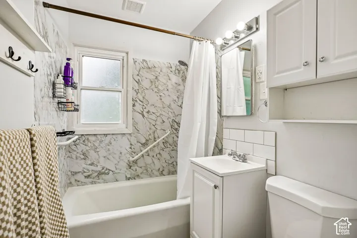 Bathroom featuring a tub/shower combination with marble-patterned surround, white subway tile backsplash, and a white vanity with integrated sink