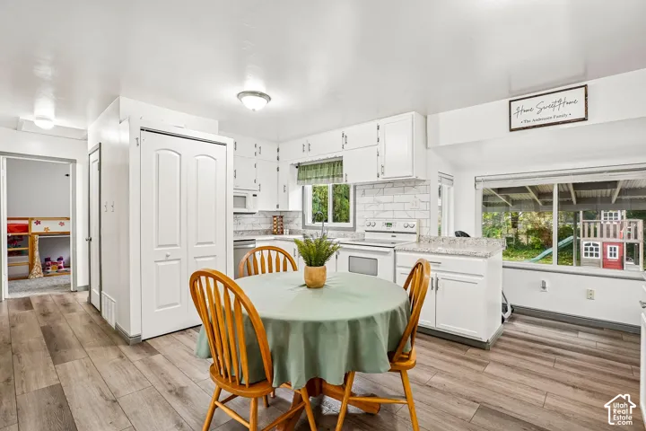 Kitchen featuring white cabinetry, light-toned countertops, white subway tile backsplash, stainless steel appliances, and wood-finish flooring