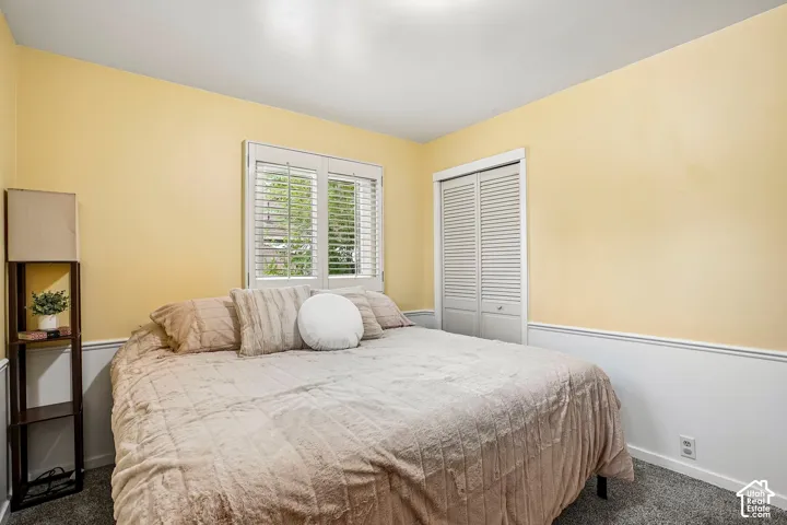 Bright and airy bedroom featuring soft yellow walls, plantation shutters on dual windows, carpet flooring, and a spacious layout ideal for furnishings and d