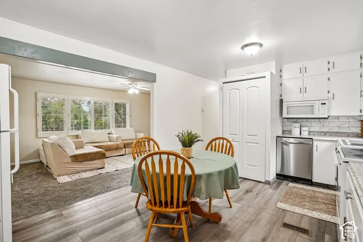 Kitchen with wood-finish flooring, white cabinetry, stainless steel dishwasher, and a white tile backsplash