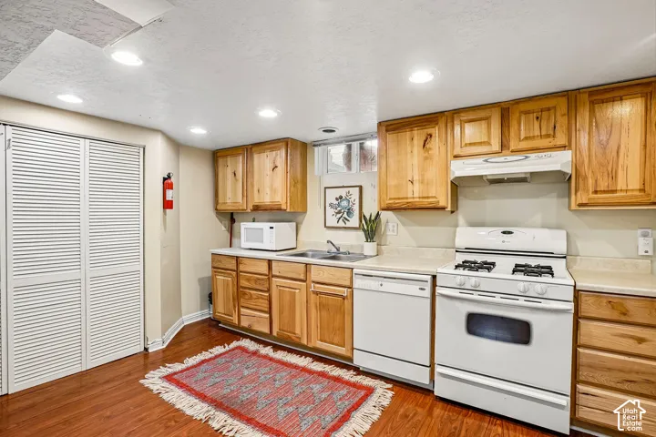 Spacious kitchen featuring warm wood cabinetry, white gas range with double ovens, stainless steel appliances, wood-finish flooring, and recessed ceiling lighting