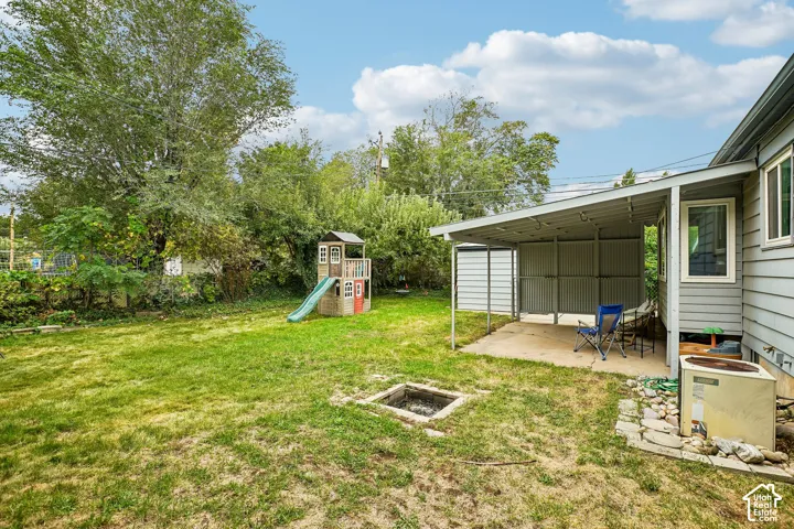 Expansive grassy yard featuring a concrete patio, covered outdoor area, and a built-in fire pit