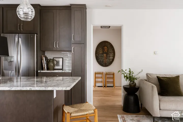 Kitchen island with a light-toned countertop, dark wood-finish cabinetry, stainless steel refrigerator, and subway tile backsplash
