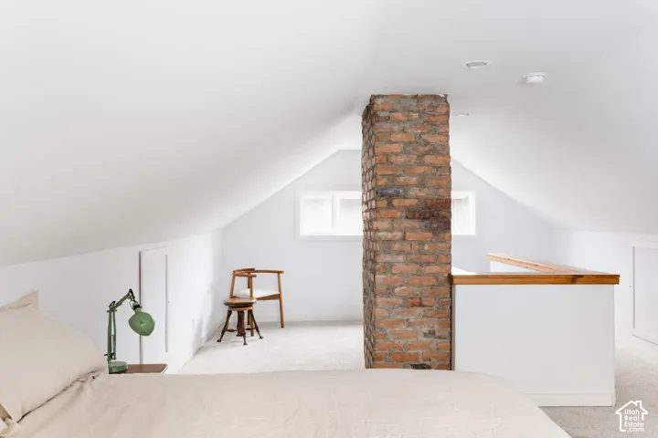 Sloped ceilings with recessed lighting, exposed brick column, light-toned carpeting, and a built-in half-wall with wood-finish top
