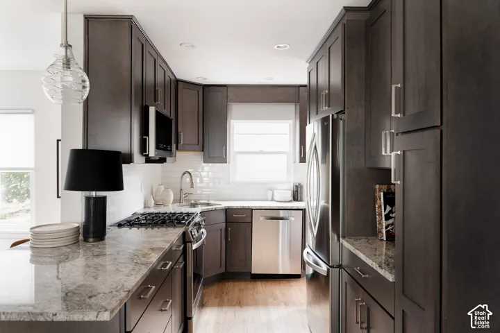 Kitchen featuring dark wood-finish cabinetry, light-toned countertops, a built-in gas range, a stainless steel dishwasher, and a built-in stainless steel refrigerator