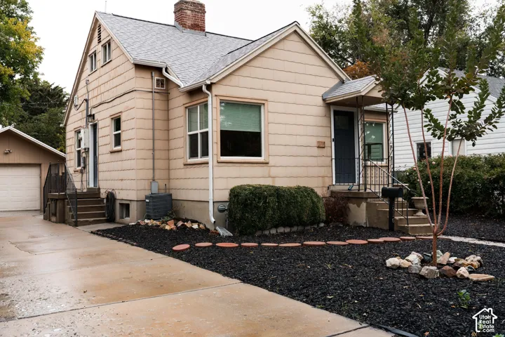 Gable-roofed home with light-colored siding, a brick chimney, and a covered front entry with wrought iron railing