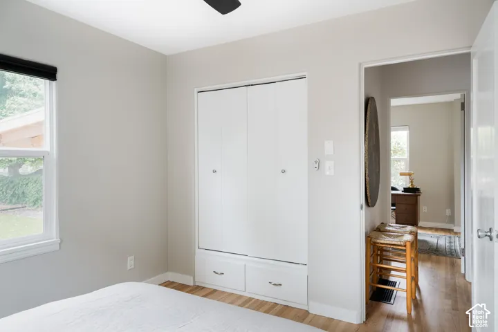 Light-colored wood-finish flooring, white built-in cabinetry with lower drawers, white window trim, and a black ceiling fan