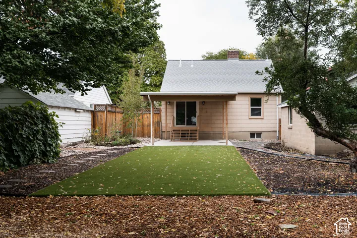 Spacious backyard featuring artificial turf, a covered patio, and mature trees
