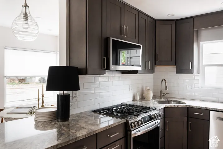 Kitchen featuring dark wood cabinetry, light-toned countertops, white subway tile backsplash, stainless steel gas range, and an undermount sink with a gooseneck faucet