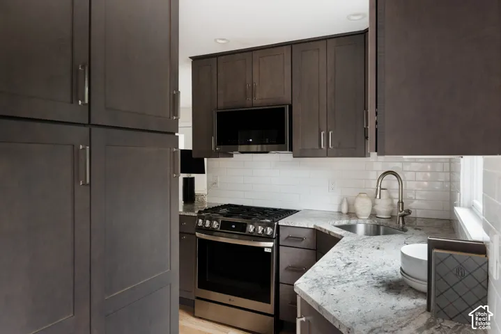 Kitchen featuring dark wood-finish cabinetry, white subway tile backsplash, stainless steel gas range, and a stainless steel sink with a high-arc faucet
