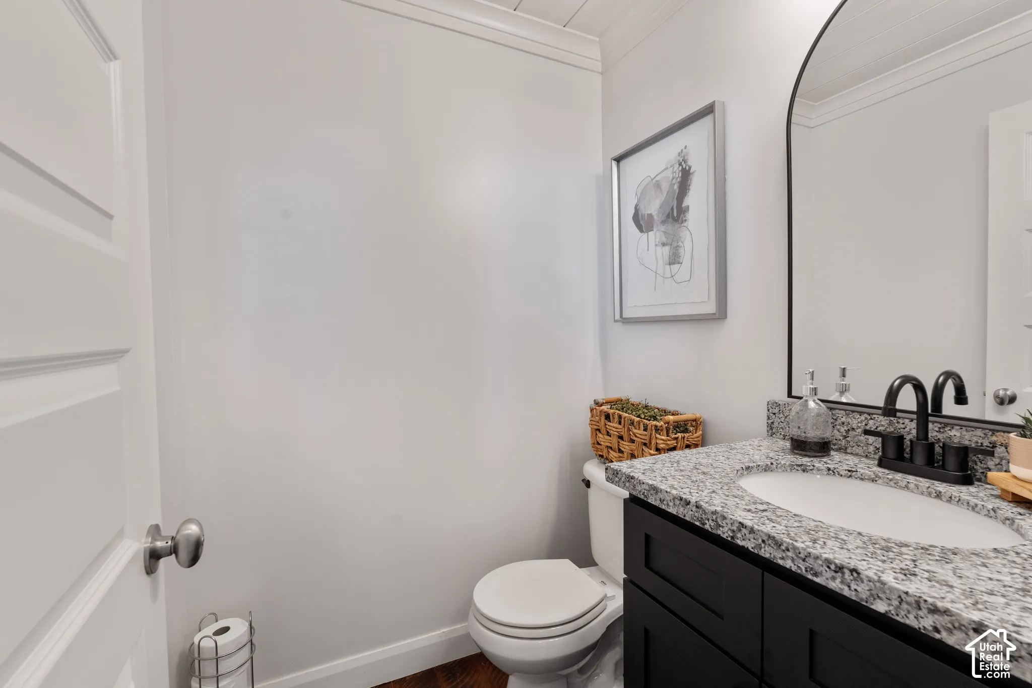 Granite countertop vanity with integrated sink, black cabinetry, matte black faucet, and arched mirror
