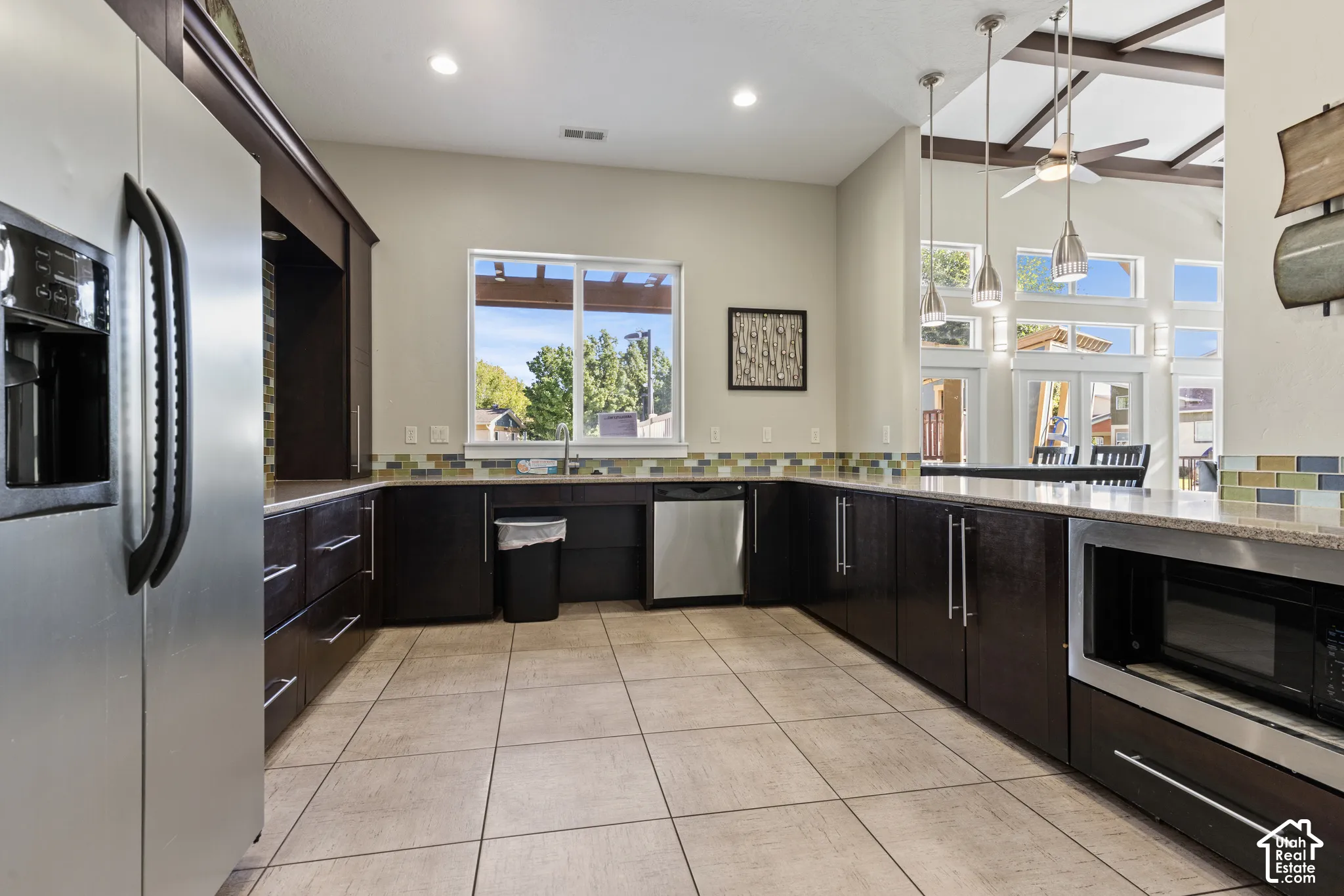 Open-concept kitchen with dark wood-finish cabinetry, tile flooring, stainless steel appliances, and a mosaic tile backsplash