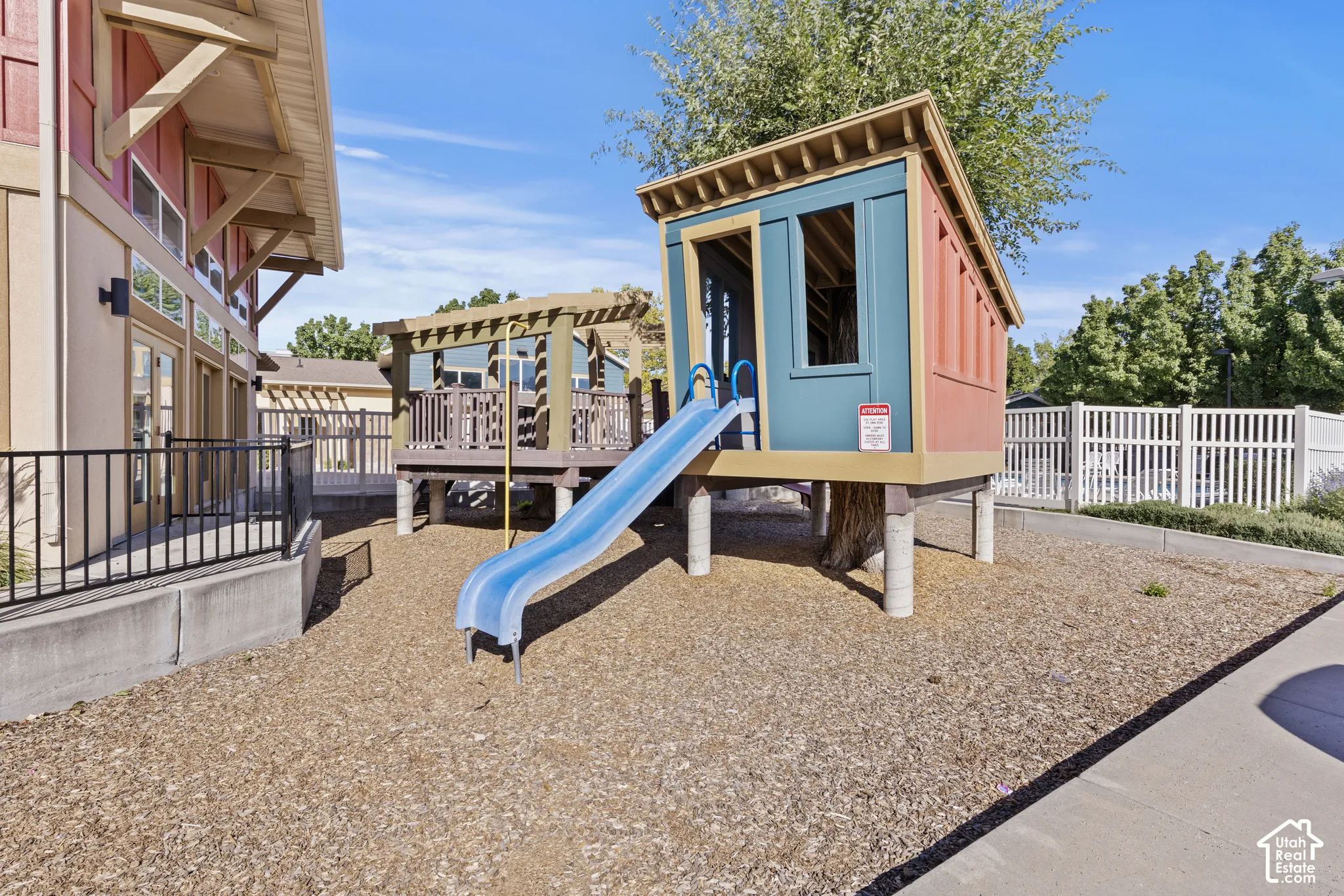 Outdoor play structure with a slide, elevated deck with a pergola, and a bark chip ground cover
