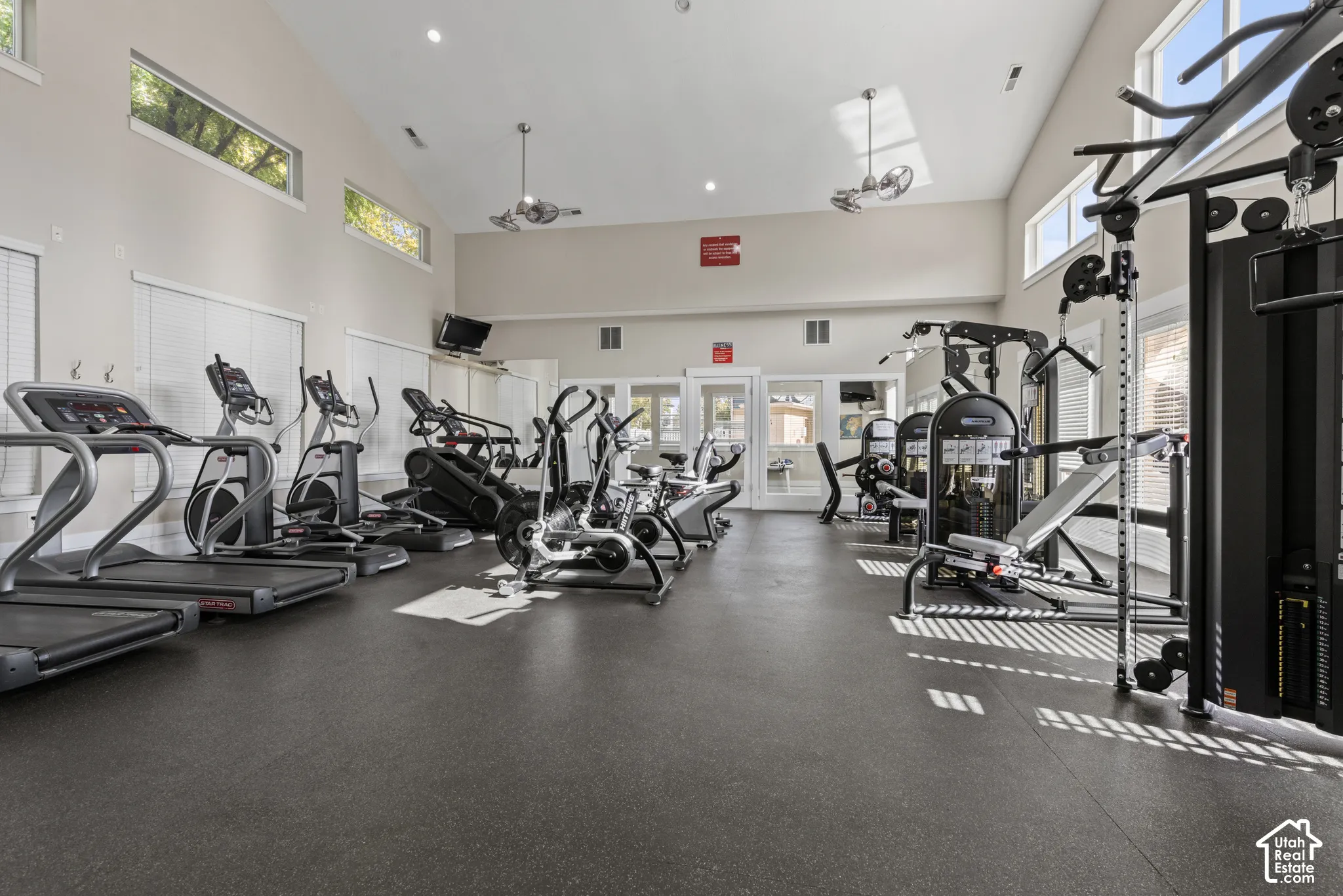 Fitness center featuring cardio and strength training equipment, high ceilings, multiple windows with blinds, and ceiling fans