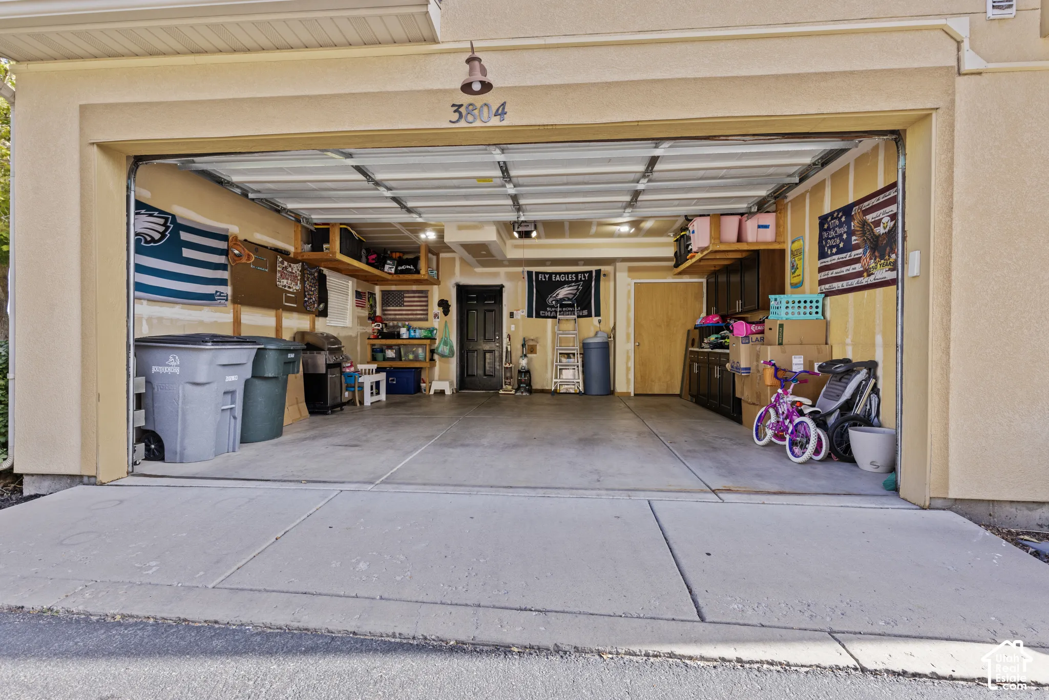 Two-car garage with concrete flooring, built-in overhead storage shelves, and overhead lighting