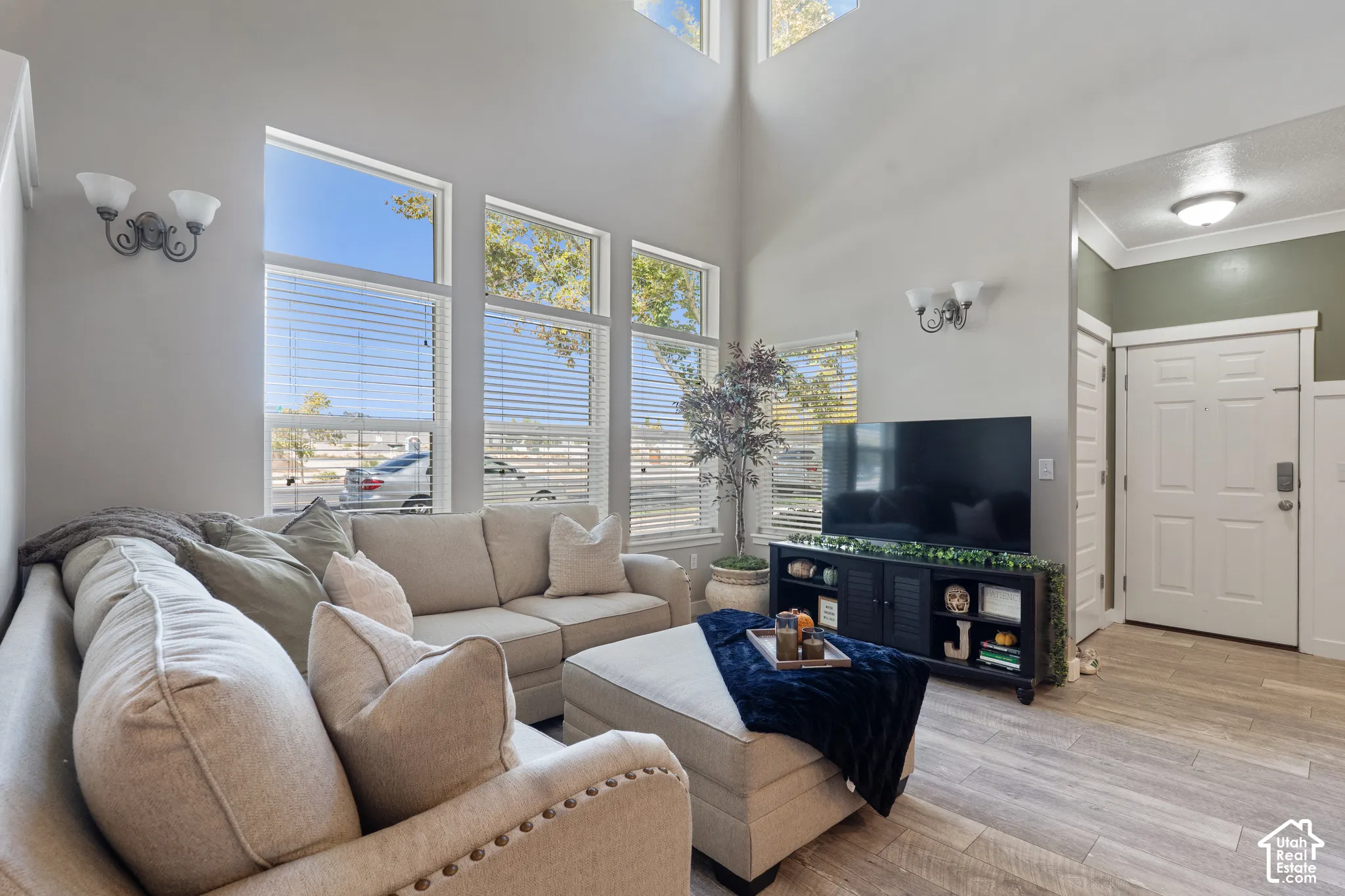 Living area featuring high ceilings, multiple tall windows with blinds, wood-finish flooring, and a paneled entry door