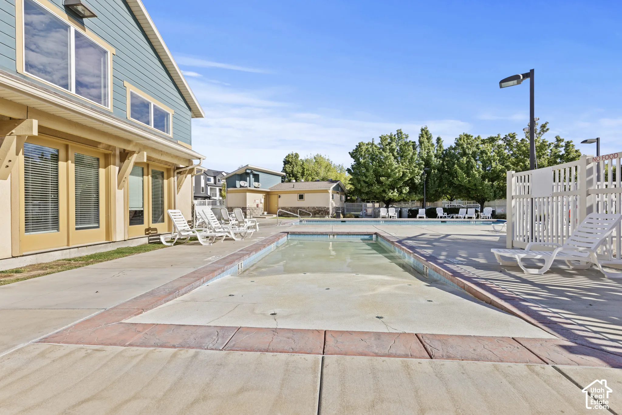 Outdoor swimming pool with integrated spa area, surrounded by concrete decking with decorative stamped border, and an adjacent building featuring large windows