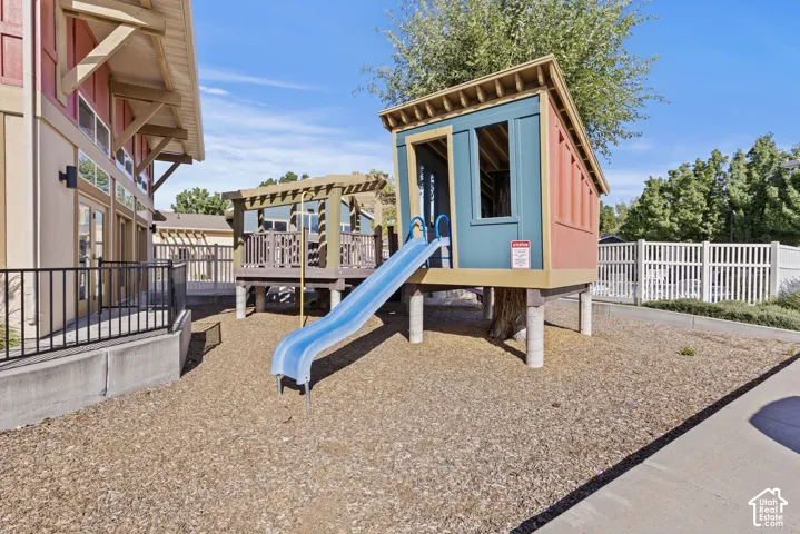 Outdoor play structure with a slide, elevated deck with a pergola, and a bark chip ground cover