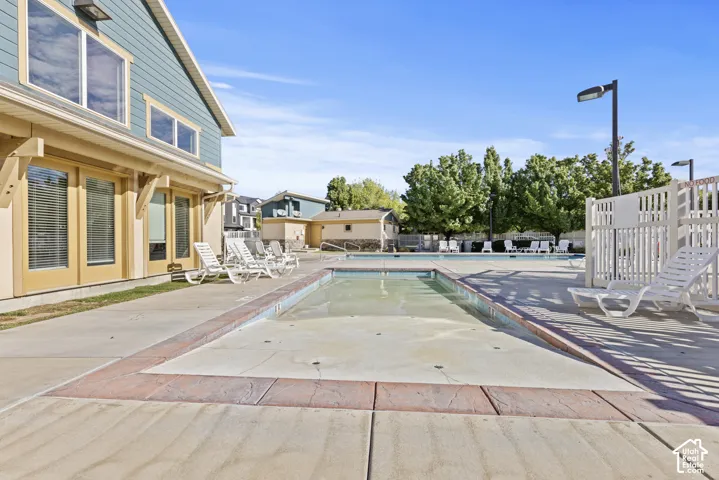Outdoor swimming pool with integrated spa area, surrounded by concrete decking with decorative stamped border, and an adjacent building featuring large windows