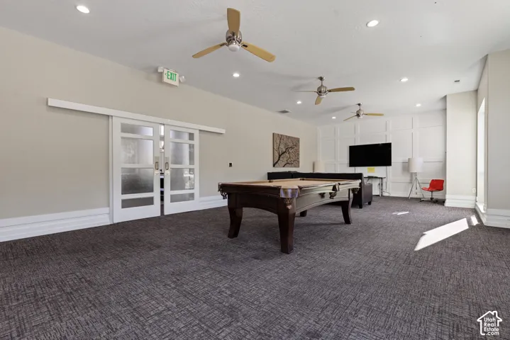 Recessed lighting and three ceiling fans illuminate the space, featuring a paneled accent wall and sliding barn doors with frosted glass