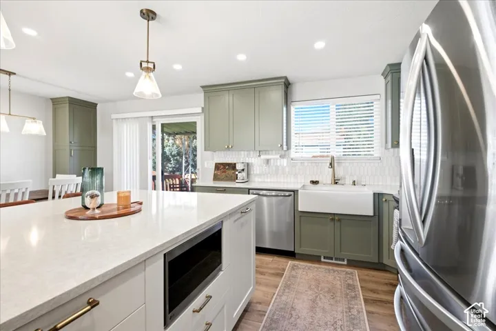 Kitchen featuring sage cabinetry, stainless steel appliances, a farmhouse sink, quartz countertops, and wood-finish flooring