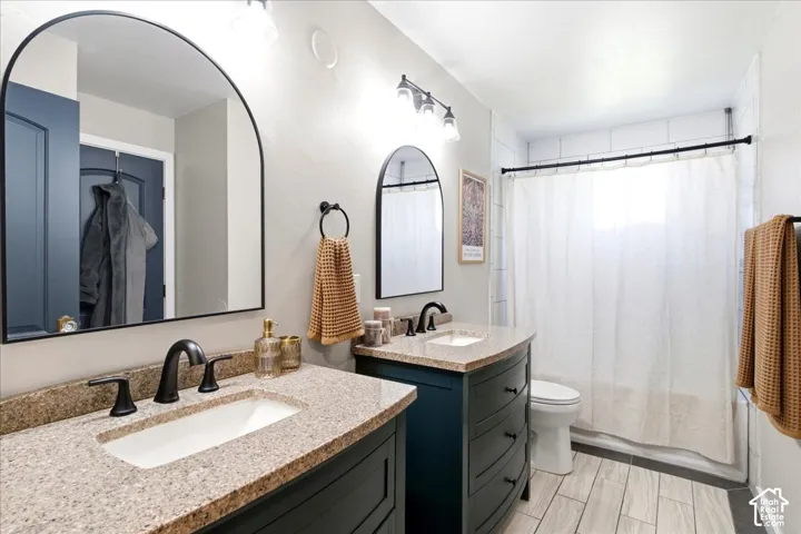 Dual arch-top mirrors, individual sink vanities with granite-style countertops, matte black plumbing fixtures, and light wood-look tile flooring