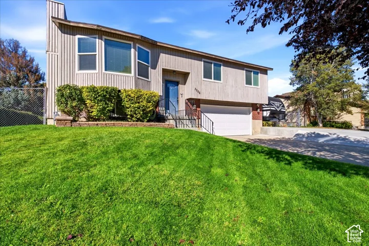 Split-level residence featuring vertical siding, an attached garage, a blue entry door, and a sloped lawn