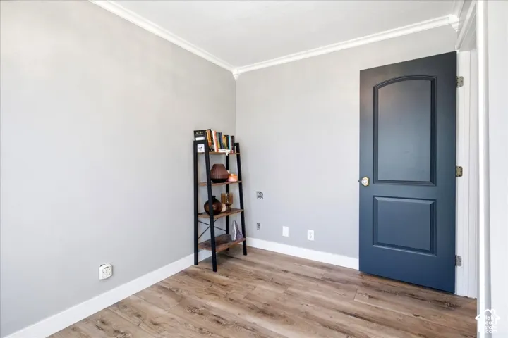 Wood-finish flooring with white baseboards, light gray walls, and crown molding
