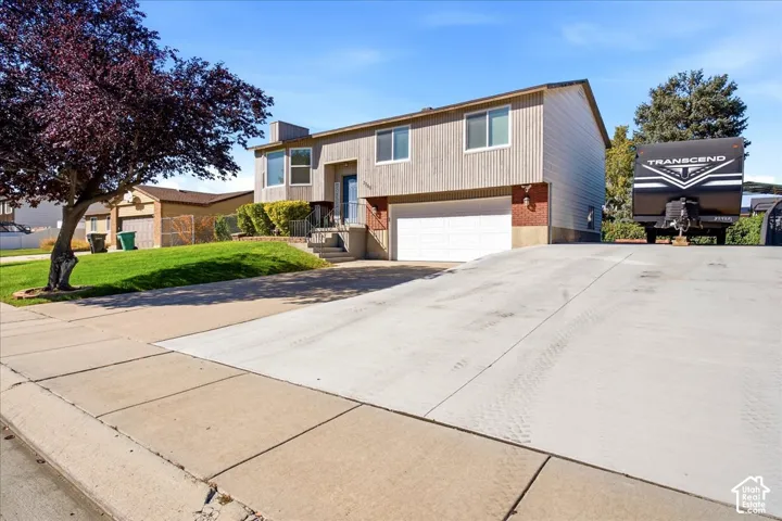 Split-level residence featuring a two-car garage, concrete driveway, and a front lawn with a mature tree