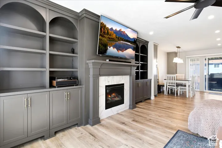Built-in cabinetry with arched shelving, fireplace with stone surround, wood-finish flooring, recessed lighting, and a ceiling fan