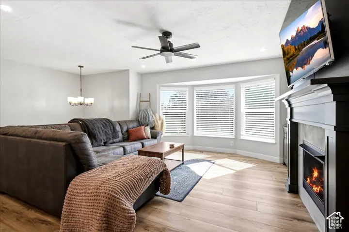 Bay window with blinds, wood-finish flooring, ceiling fan, recessed lighting, and a built-in fireplace with mantel